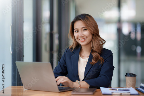 Happy young asian businesswoman sitting on her workplace in the office. Young asian woman working at laptop in the office.