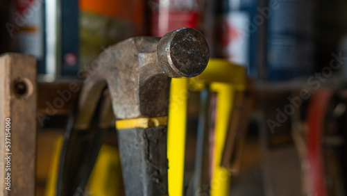 Martillo de hierro acero colgado en una repisa de herramientas, con mango de goma de color negro y amarillo , rodeado de herramientas y latas de pintura