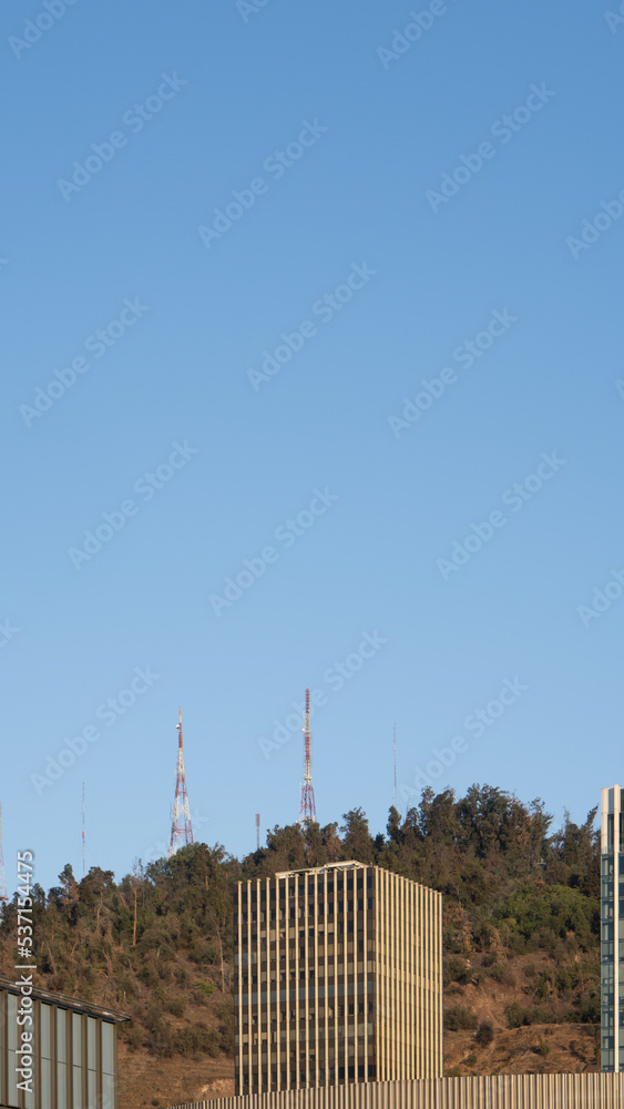 Fototapeta premium Vista de un edificio con cielo azul. De fondo un cerro con antenas de comunicación