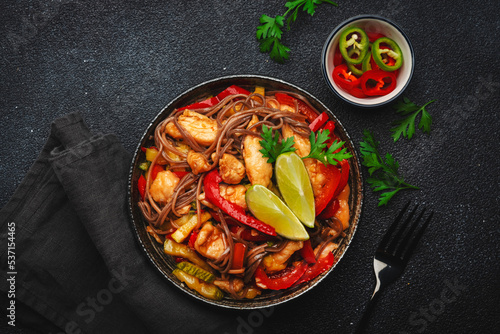 Asian cuisine, stir fry noodles with chicken and vegetables and sesame seeds in bowl. Black kitchen table background, top view, copy space