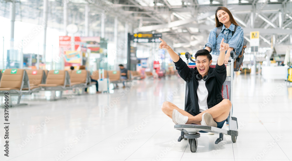 Happy smiling asian male and female waiting for flight and Check-in by mobile phone in terminal background.asian couple are traveling after the coronavirus 2019 (COVID-19) outbreak ends.