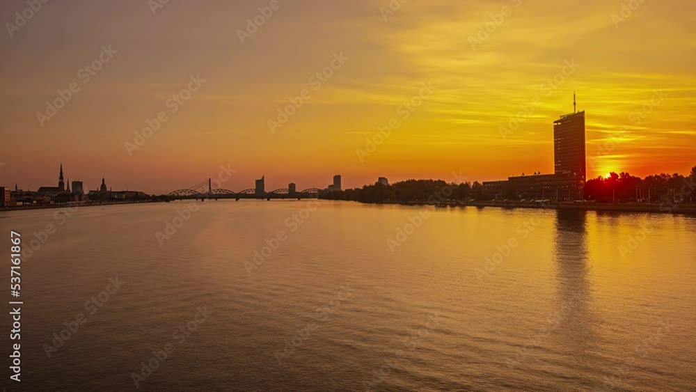 Sunrise over the Daugava River in Riga. Beautiful epic time-lapse of sun rising behind buildings and reflection in water. 