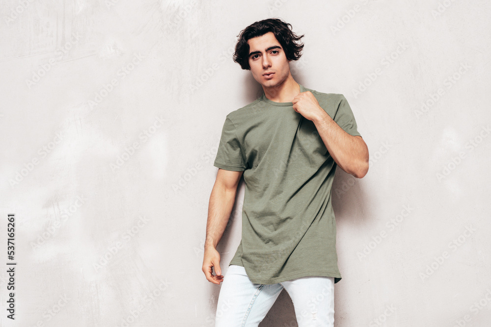 Portrait of handsome confident stylish hipster lambersexual model.Sexy man dressed in over size T-shirt and jeans. Fashion male isolated in studio. Posing near grey wall Portrait of handsome confident stylish hipster lambersexual model.Sexy man dressed in over size T-shirt and jeans. Fashion male isolated in studio. Posing near grey wall