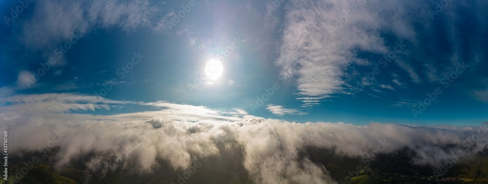 Aerial panoramic view from between low clouds, illuminated by the sun, at sunrise. Captured using a drone.