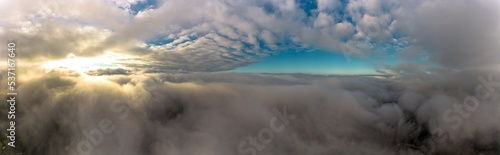 Aerial panorama view from between low clouds, illuminated by the sun, at sunrise. Captured using a drone.