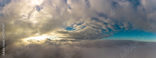 Aerial panorama view from between low clouds, illuminated by the sun, at sunrise. Captured using a drone.