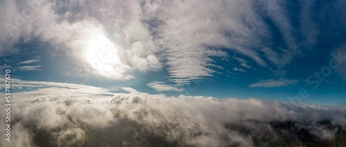 Aerial panoramic view from between low clouds  illuminated by the sun  at sunrise. Captured using a drone.