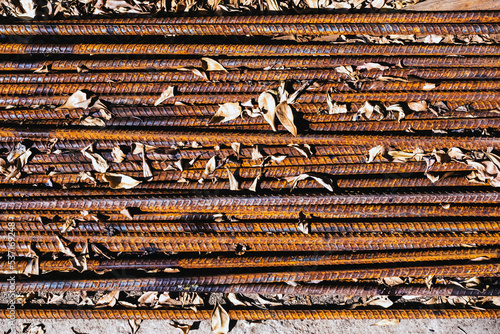 Top view old rusted iron bars and dry leaves on floor. Close up to stack of straight old rusty steel reinforcement structural steel bars from construction site. Steel rod with rust. Rusty Metal Bars.