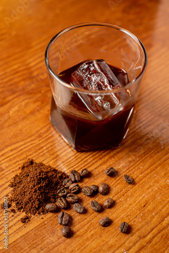 refrescante café helado en un vaso junto a granos de café sobre una superficie de madera