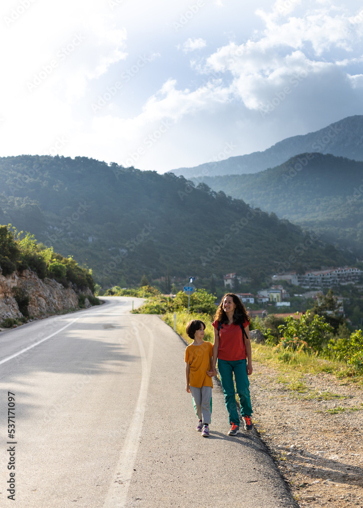 A boy and his mother are walking along the road against the backdrop of mountains