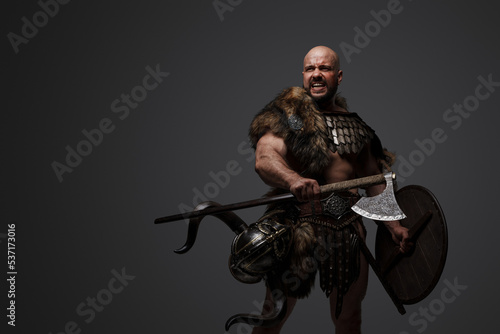 Portrait of violent barbaric viking dressed in armor and fur holding shield and axe.