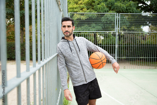 Man leaning on a fence in a public basketball court photo