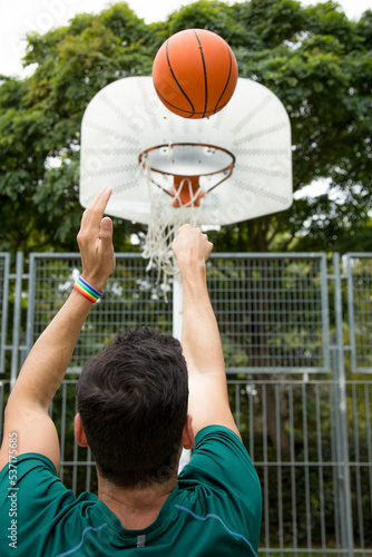 Vertical photo of a man with a rainbow bracelet playing basketball court