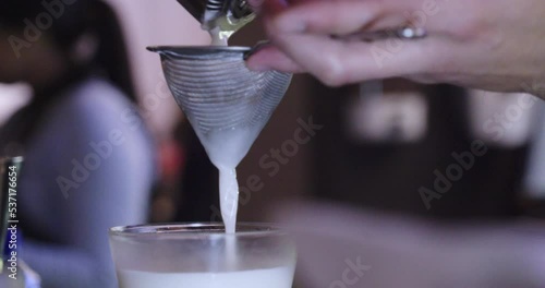 Elegant bartender pouring ingredients into a glass through a strainer to prepare a drink in a bar at night. photo