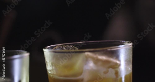Close-up of orange juice being poured by an elegant bartender into glasses with ice for drink presentation in a bar at a night party. photo