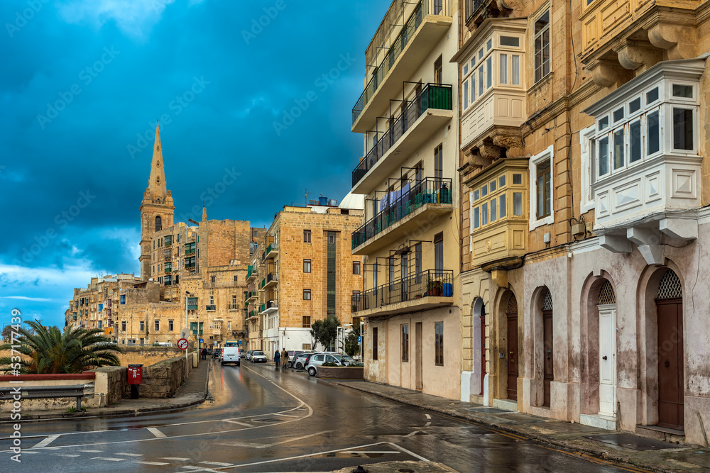 Fototapeta premium Traditional buildings and church under cloudy sky in Valletta, Malta.