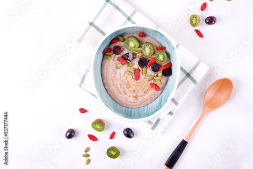 Fotografie Creamy farro porridge served with mini kiwi, grape, goji berries and pumpkin seeds in bowl