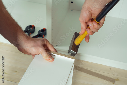 Wallpaper Mural Male hands hold metal hammer with yellow plastic handle, driving dowel, assembling white drawer of dresser or wardrobe. Self-assembly of furniture at home, DIY, furniture repair and rearrangement Torontodigital.ca