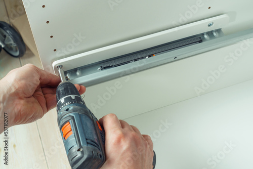 Wallpaper Mural Male hands hold cordless electric screwdriver, screw to fix rail, assembling drawer of white dresser or wardrobe. Self-assembly of furniture at home, DIY, furniture repair and rearrangement Torontodigital.ca