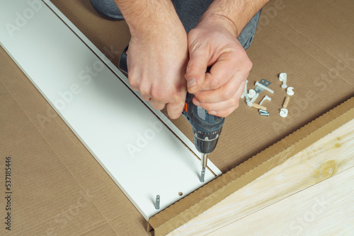 Wallpaper Mural Male hands hold cordless electric screwdriver, screw to fix walls of white drawer, assembling dresser or wardrobe on floor. Self-assembly of furniture at home, DIY, furniture repair and rearrangement Torontodigital.ca