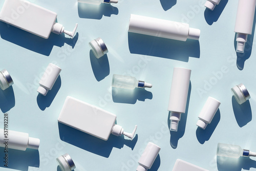 Pattern made with white bottles and jars of cosmetic products and strong shadow on blue background, as backdrop or texture. Creative layout for your design