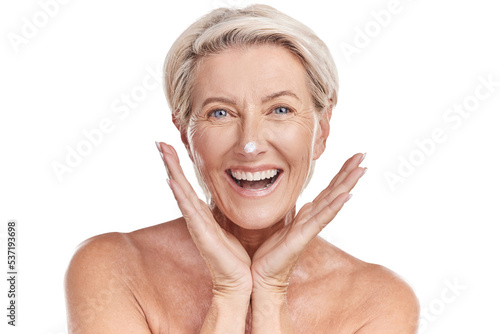 Portrait of one happy mature caucasian woman posing topless against a purple copyspace background. Ageing woman applying cream  moisturiser  sunblock during a skincare routine in a studio