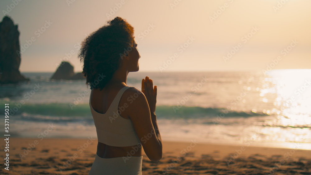 Back view woman meditating sitting with namaste hands in front sunrise close up.