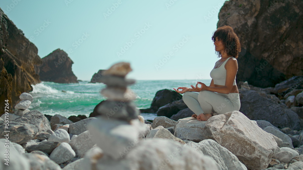 Woman meditating sitting lotus pose on stone Ursa beach. Girl practicing yoga.