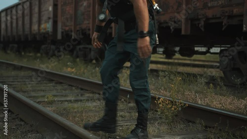 Bodybuilder with balloon drager on his back is training at railway yard and quickly pulls knees to chest leaning his hands on the rails photo