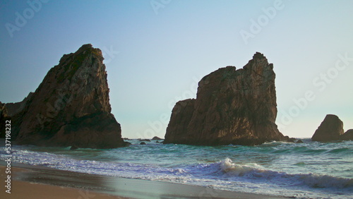 Rocky cliffs rising ocean surface on Portugal Ursa beach summer evening.