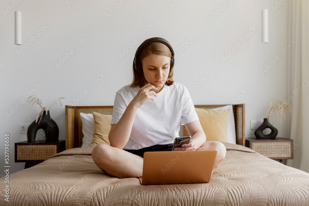 A young woman sits on a bed and takes online training, checks mail or messages on a social network. Home online learning concept A young woman sits on a bed and takes online training, checks mail or messages on a social network. Home online learning concept
