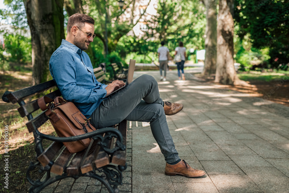 Fototapeta premium Joyful entrepreneur or businessman, sending an e-mail from the park bench.