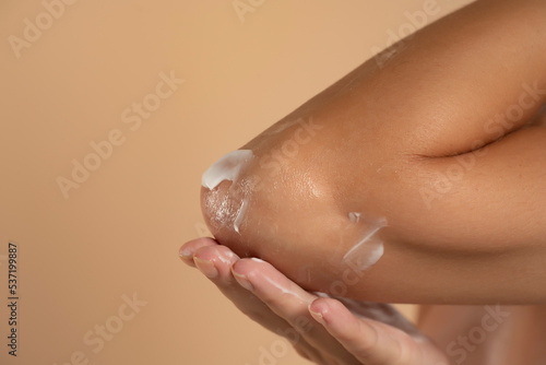 Close-up of a woman takes care of his elbows using cosmetic cream on a beige background