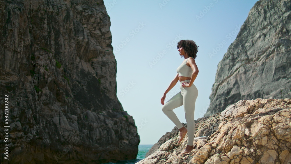 Woman making yoga asana standing rocky beach. African american girl stretching.