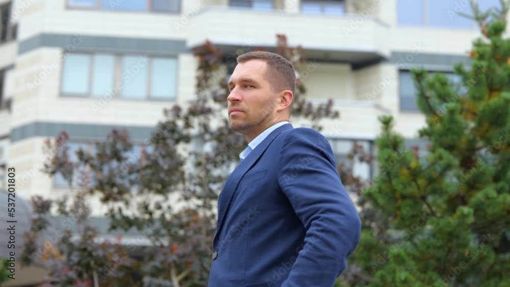 Rear view. Close up of young happy confident man in suit standing outdoors turning to camera and smiling. Positive Caucasian businessman posing on street. Business concept Rear view. Close up of young happy confident man in suit standing outdoors turning to camera and smiling. Positive Caucasian businessman posing on street. Business concept