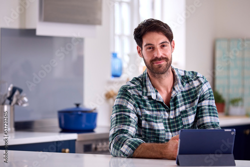 Portrait Of Man Using Digital Tablet In Kitchen To Work From Home Book Holiday Or Shop © Monkey Business