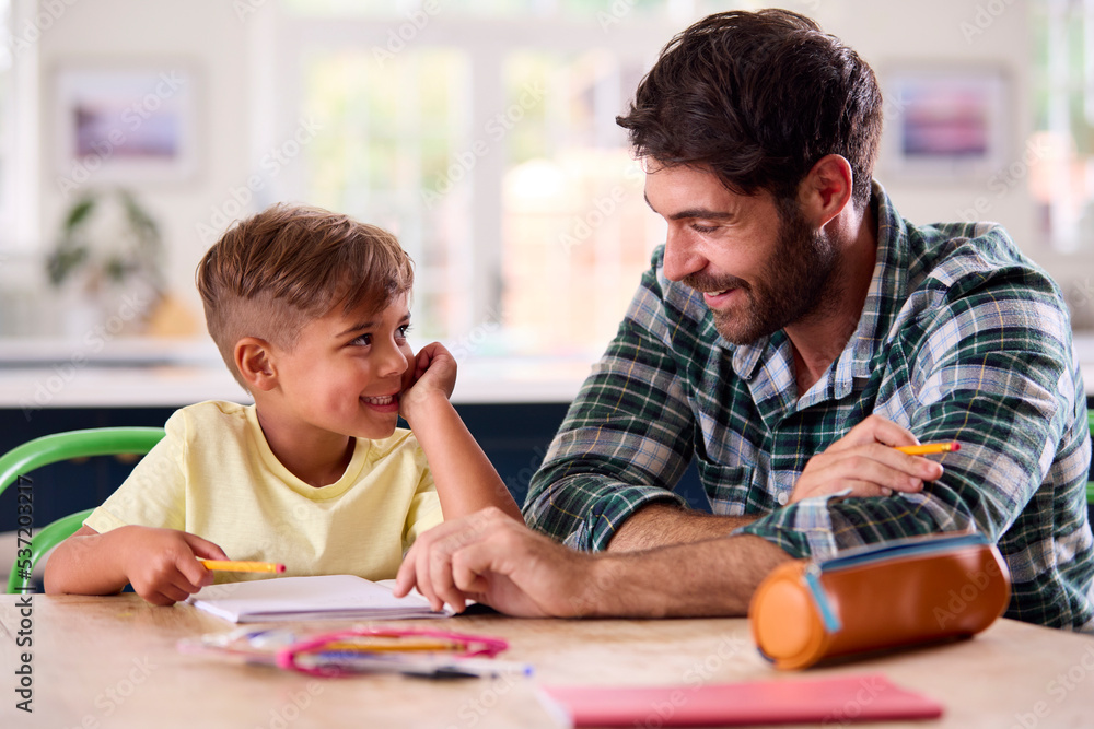 Father At Home In Kitchen Helping Son With Homework