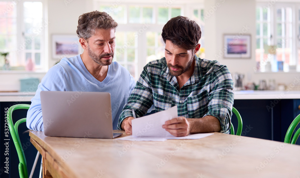 Same Sex Male Couple Using Laptop At Home To Check Domestic Finances Same Sex Male Couple Using Laptop At Home To Check Domestic Finances