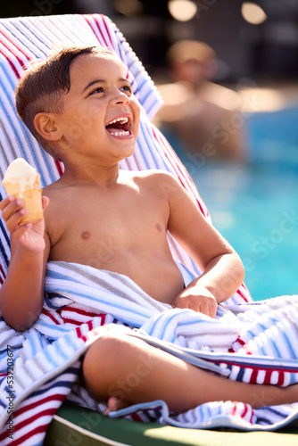 Boy On Summer Holiday On Lounger By Swimming Pool Eating Ice Cream