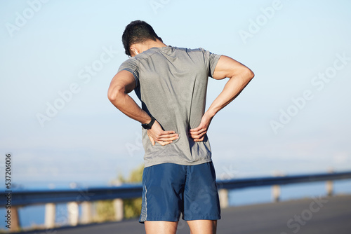 Fitness, tired and man with back pain in city while training cardio, marathon and health. Athlete runner with medical emergency for body while running, doing sports exercise and workout in the street
