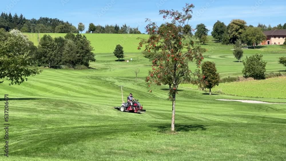 green keeper on lawn tractor mowing fairway on golf course green keeper on lawn tractor mowing fairway on golf course
