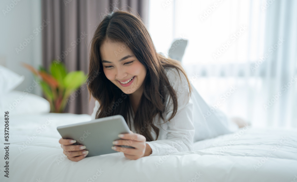 Girl lying in bed playing tablet computer in bedroom With a smiling face