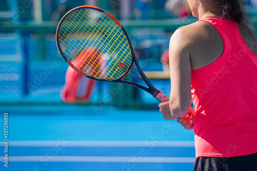 A girl plays tennis on a court with a hard blue surface on a summer sunny day