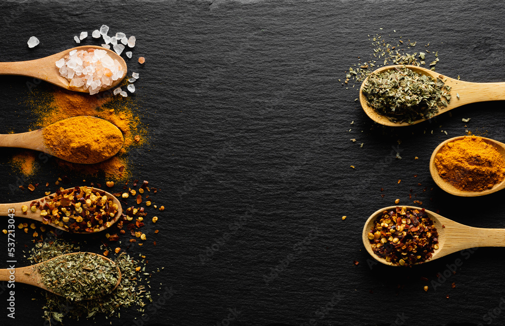 Colored spices on wooden spoon  on slate dark background with copy space