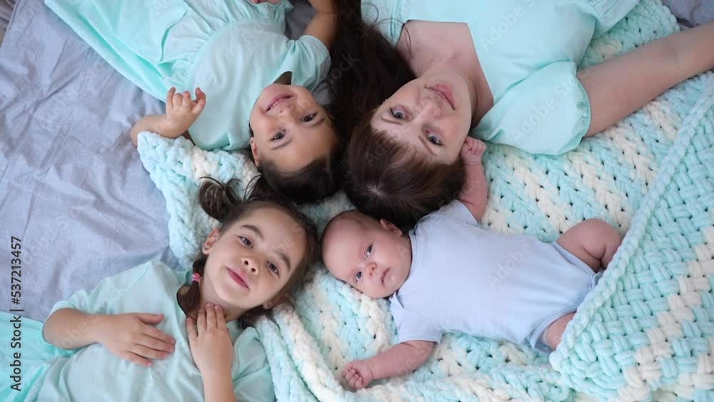 Young beautiful mother with her daughters and newborn baby lying in bed at home. Young beautiful mother with her daughters and newborn baby lying in bed at home.