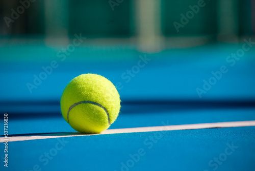 a tennis ball lies on a white marking on a blue hard court