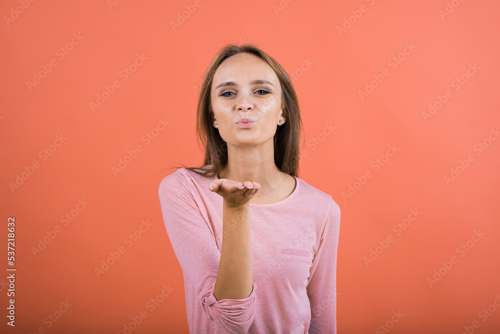 The girl shows with her lips the gesture of an air kiss on a red background. The girl shows with her lips the gesture of an air kiss on a red background.