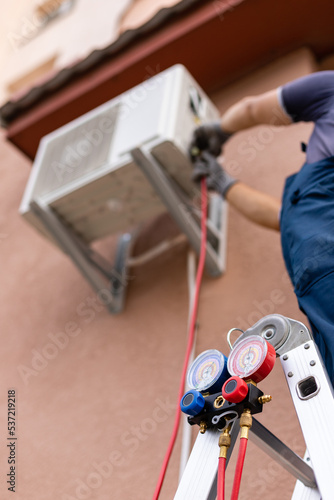 Worker maintains outdoor air conditioner using manometers for filling air conditioners.