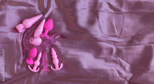 Pink silicone sex toys on a pink silk background. An erotic toy for entertainment. Various anal butt plugs. Banner with space for text