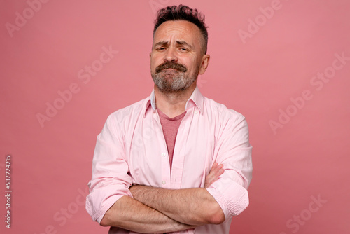 Portrait of doubtful man in pastel pink shirt on pink wall. Middle age grey-haired beard man with crossed hands thinking about question, pensive expression. smiling with thoughtful face. doubt concept photo